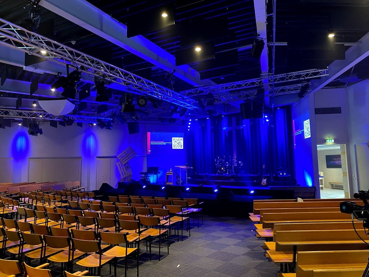 De hoofdzaal van Z1 Verhuur met podium, lichttruss en rijen stoelen, uitgelicht in blauw