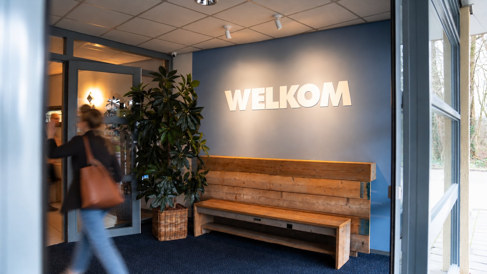 Een gast loopt binnen bij de entree van Z1 Verhuur, met de verlichte letters WELKOM boven de houten bank