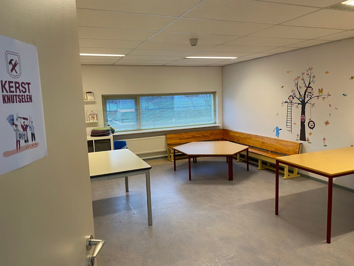 Kleine zaal met losse tafels en een houten wandbank onder het raam