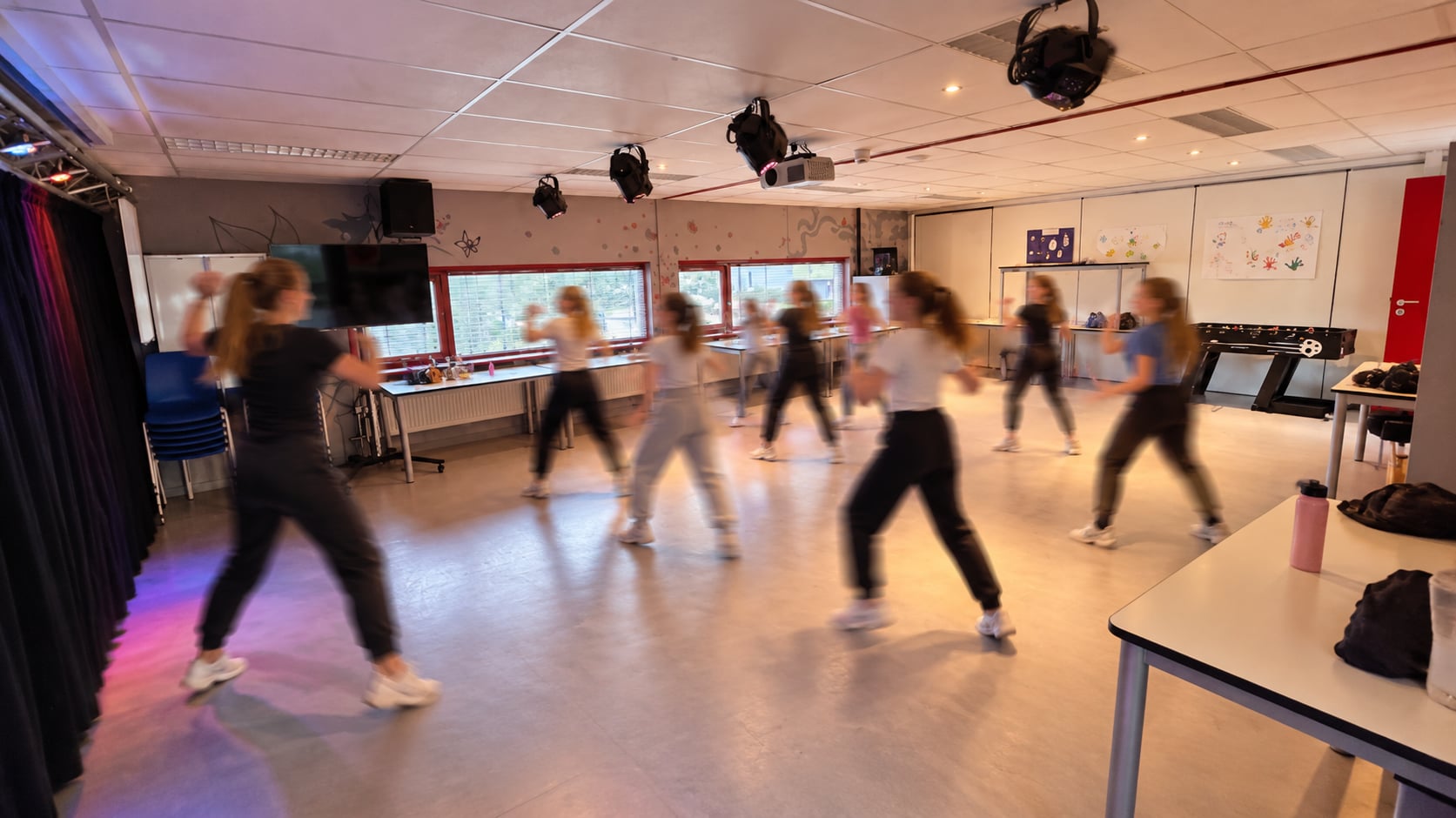 Een dansles in de multifunctionele ruimte: vrije vloer, spots aan het plafond en daglicht door de ramen