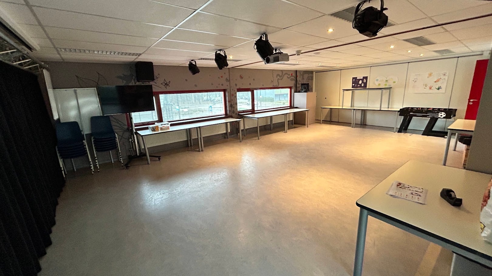 De multifunctionele ruimte met een vrije vloer, verrijdbare tafels langs de wand, tv-scherm, beamer en spots aan een truss