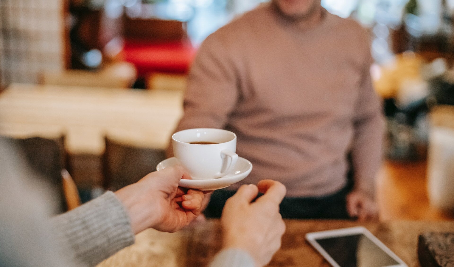 Twee mensen geven elkaar een kop koffie aan in de ontmoetingsruimte